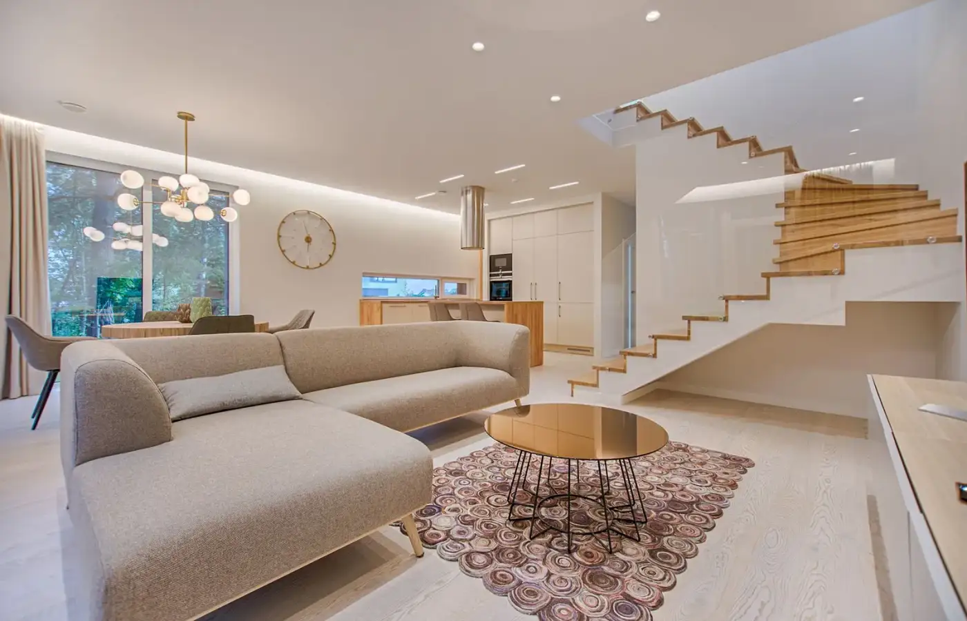 A light living room with a fabric sofa, a timber stair, and tall windows