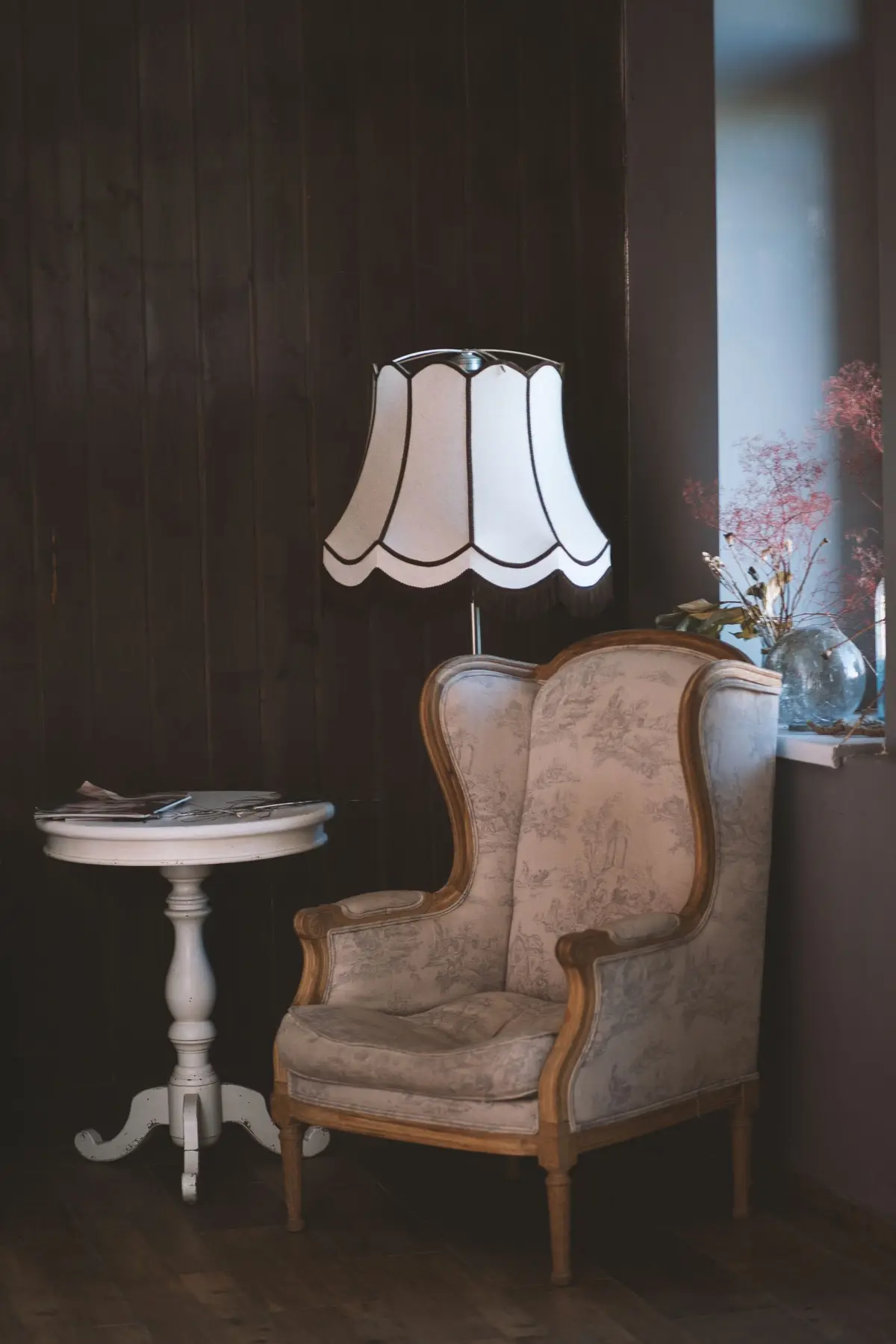 An upholstered wing chair with a timber frame beside a window and a small round table