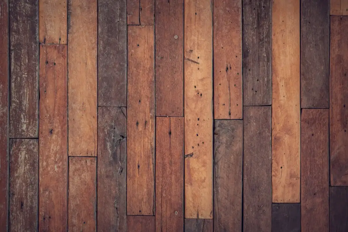 Weathered timber boards in mixed brown tones with scratches, nail holes, and worn patches